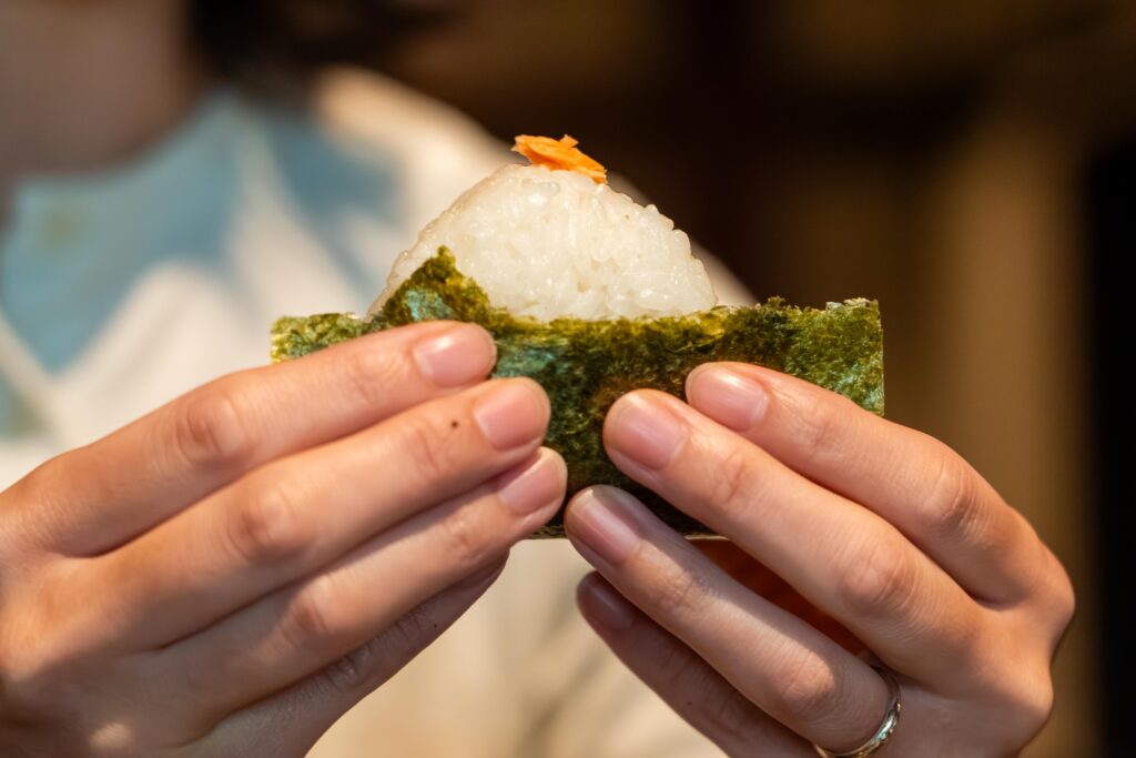 南魚沼産コシヒカリを使った「こめのすけ」のおにぎり。手に持つと粒の立つツヤがわかる、塩むすびのアップ写真。