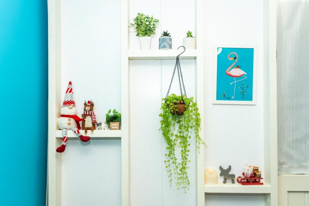 DIYで作られた白い飾り棚。観葉植物やフラミンゴのアート、サンタクロースの人形などが飾られた、おしゃれな内装ディテール。