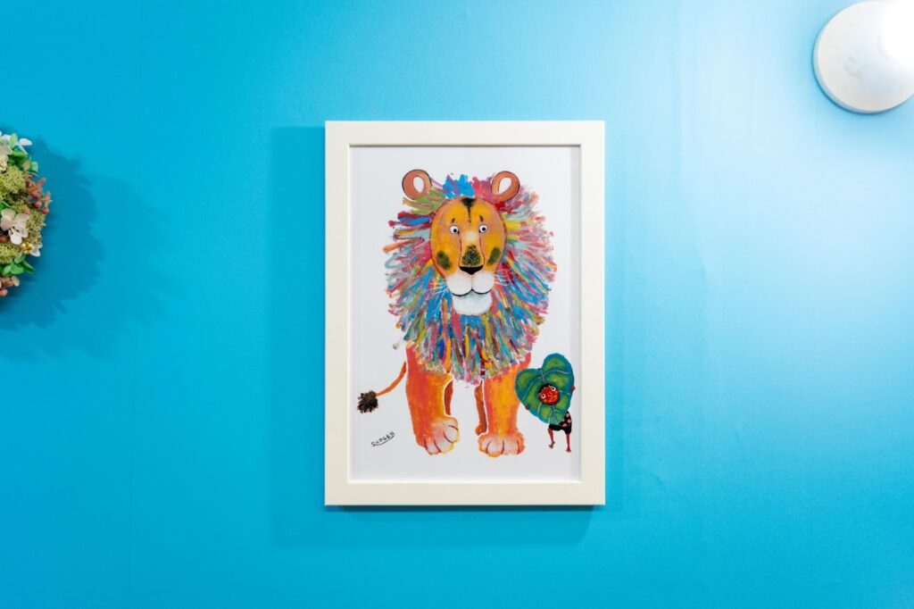 店内のブルーの壁に飾られた、カラフルなライオンのイラストのアートフレーム。明るく温かい店内の雰囲気。